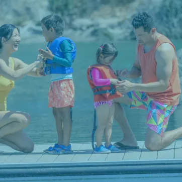 Photo shows family putting on life jackets near water.